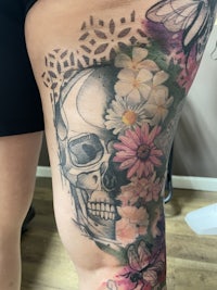 a woman's thigh tattoo with flowers and a skull